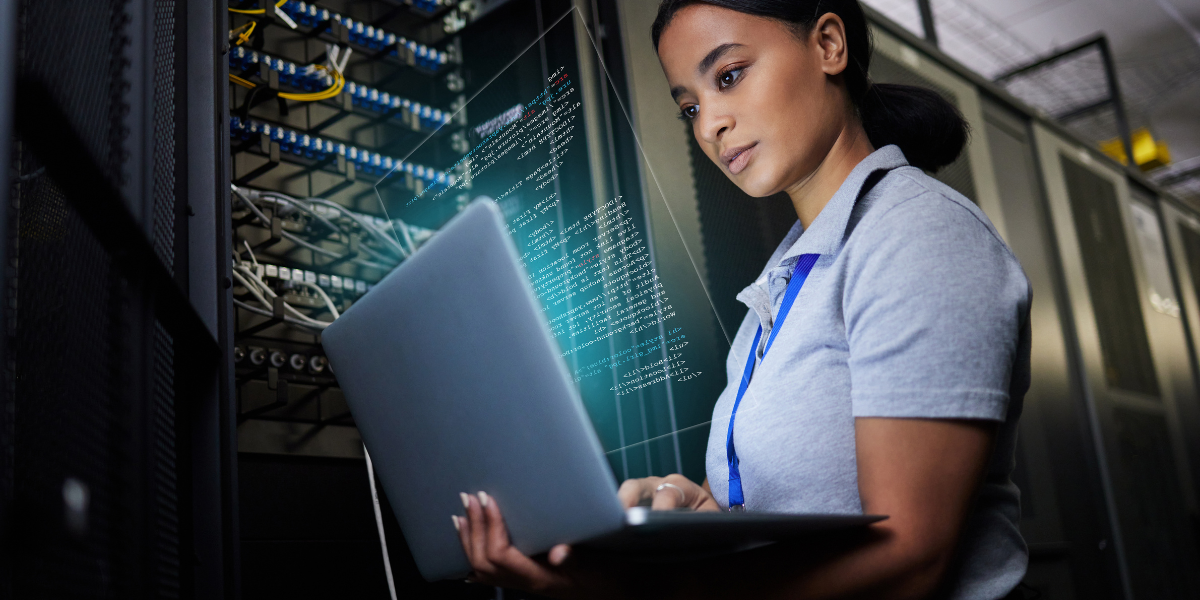 Woman IT technician with laptop performing server maintenance in data centre with network cables and server racks visible