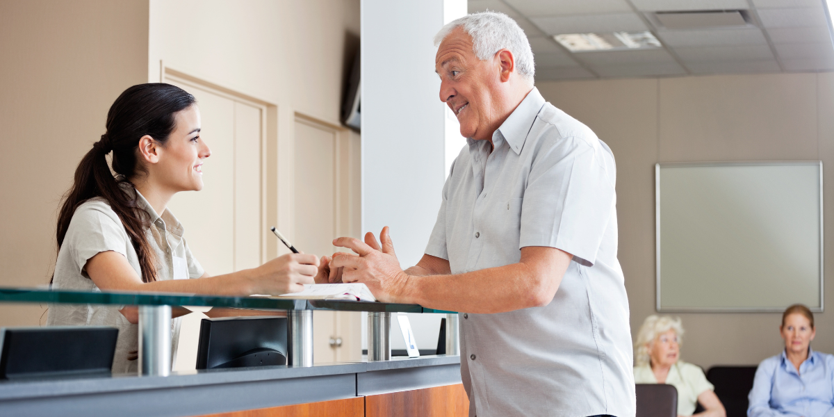 A dedicated medical secretary helps an elderly man check into his appointment, showcasing the essential patient-facing skills required to become a medical secretary in Cork.