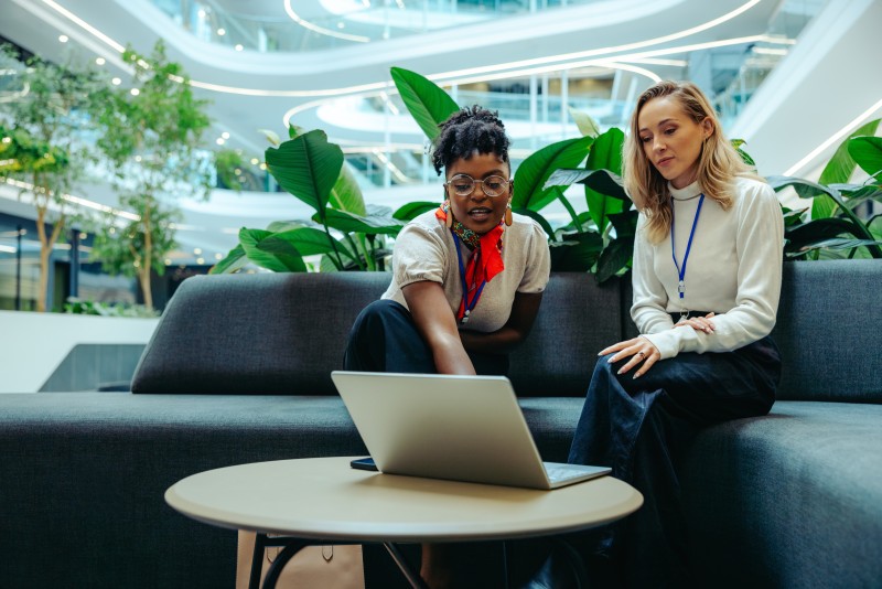 Two professional women collaborating on a laptop in a modern sustainable office environment, representing Pitman Training’s Sustainability in Business Award.