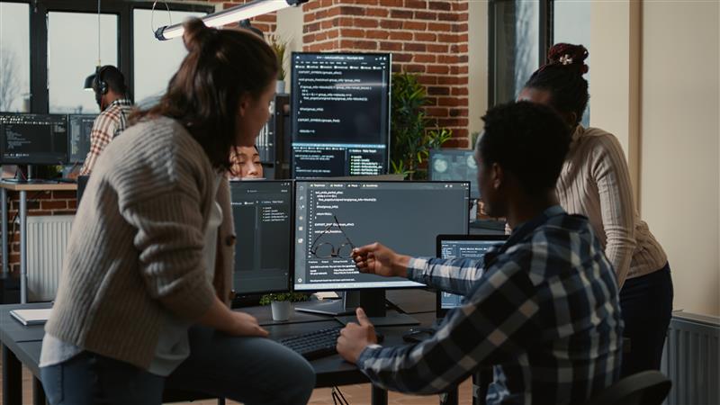 Group of learners collaborating on computer programming during IT training diploma course